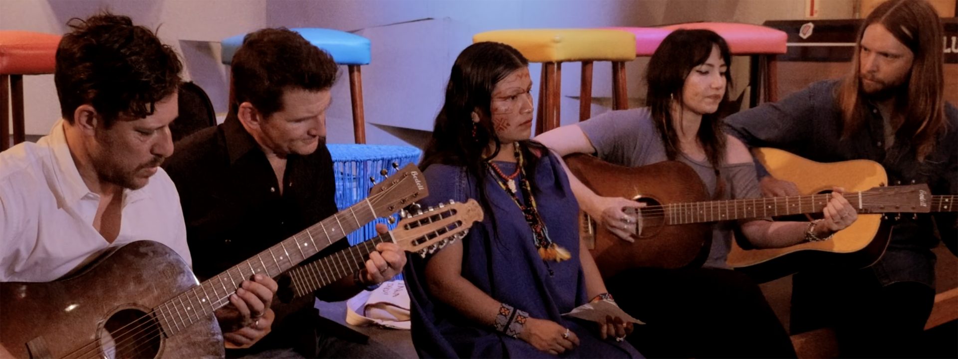 Musicians play guitars next to a tattooed person in Indigenous clothing
