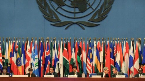 A row of country flags behind a long desk of speakers