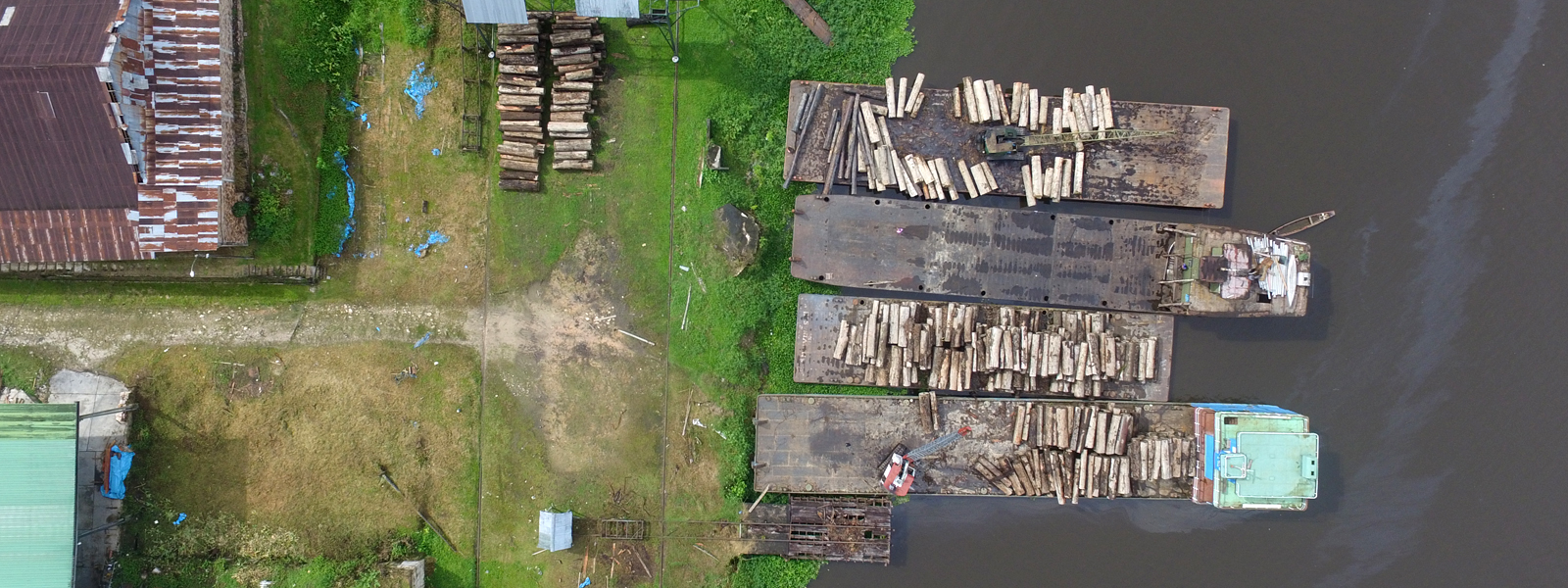 Boats on a riverbank are piled with logs