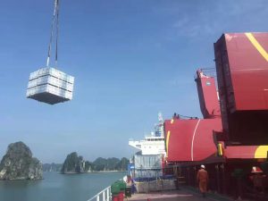 A crane lifts a container of plywood onto a ship