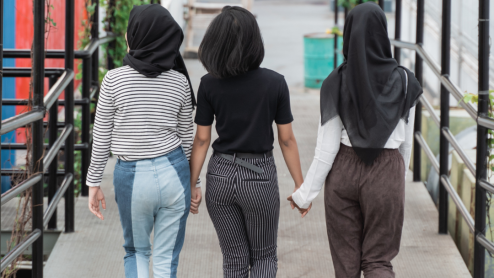 A group of women, two wearing hijabs, walk down a street holding hands