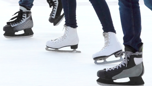 A close-up of the skates of three people on ice