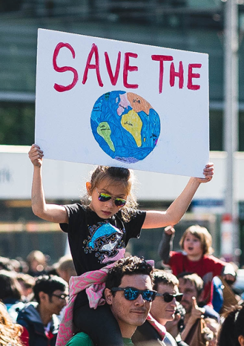 A child on a man's shoulders holds up a sign calling to save the Earth