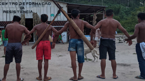 A group of Indigenous environmental defenders lock arms to form a chain. The two men in the middle have long quivers of arrows on their backs