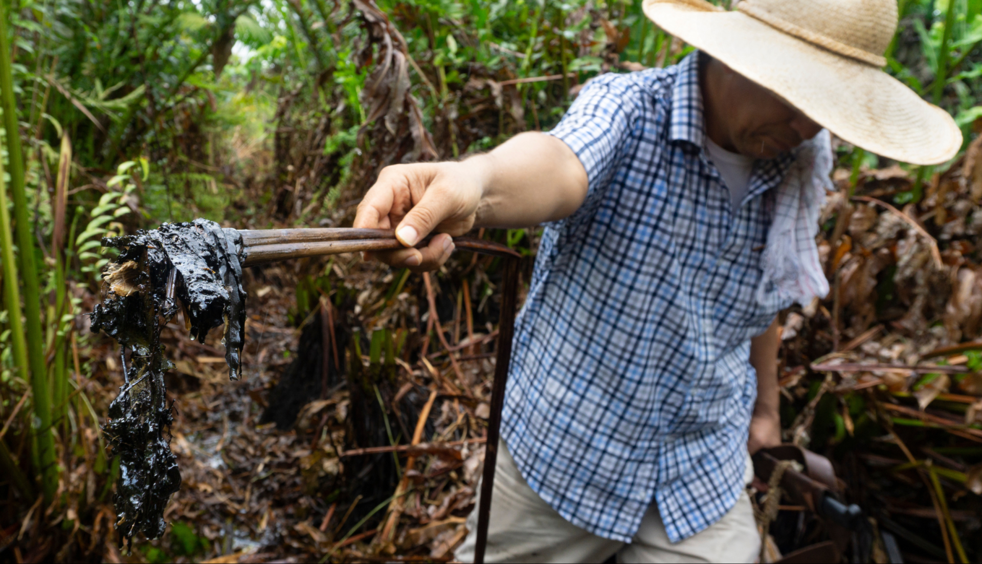 A man with a straw hat holds out a stick covered in pollution