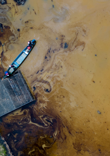 A blue canoe stands out against murky water swirling with black oil