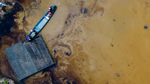 A blue canoe stands out against murky water swirling with black oil