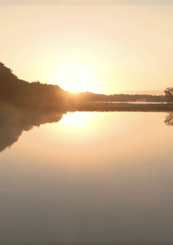 The sun rises over a still body of water