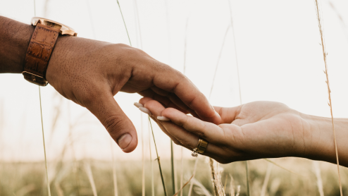 Two people hold hands in a grassy field