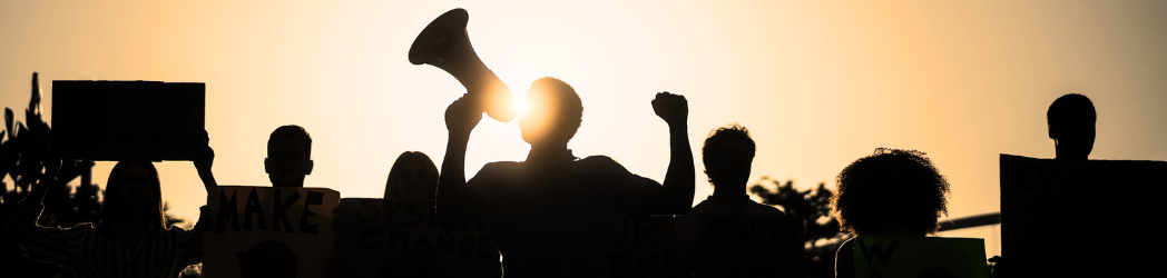 A group of protestors holding signs, silhouetted against the sun
