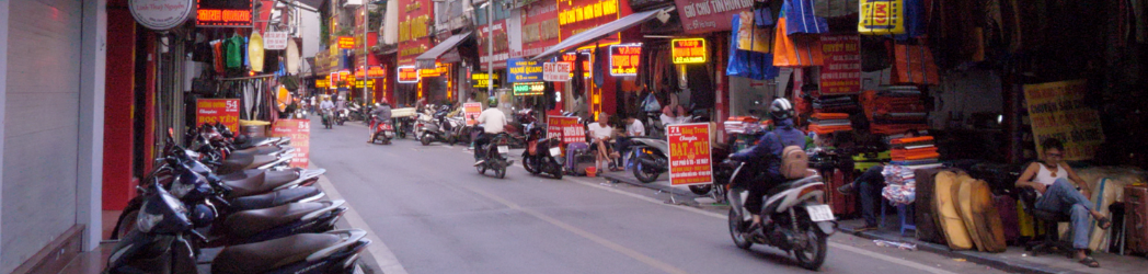 Motorbikes travel down a narrow lane lined with shops