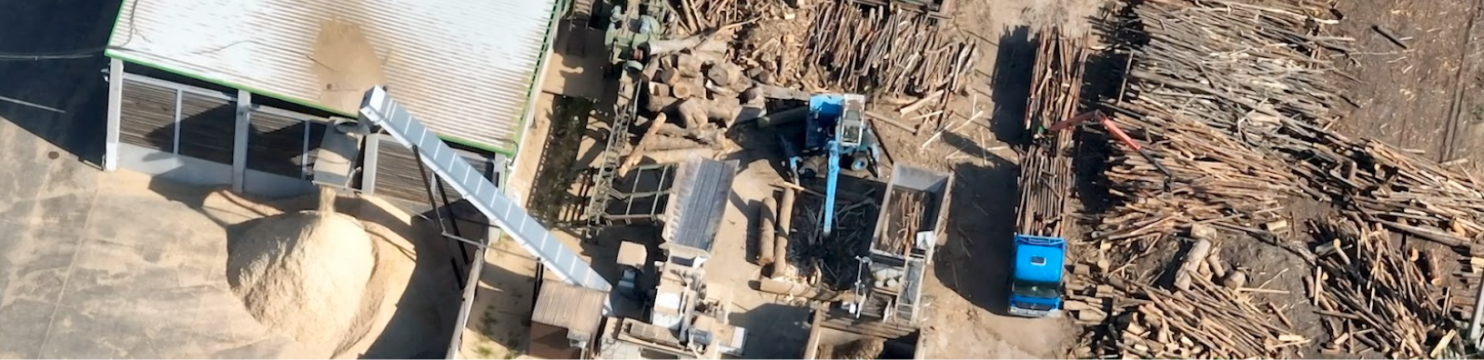 An aerial view of piles of logs surrounding a tall wood chipper dropping sawdust into a pile